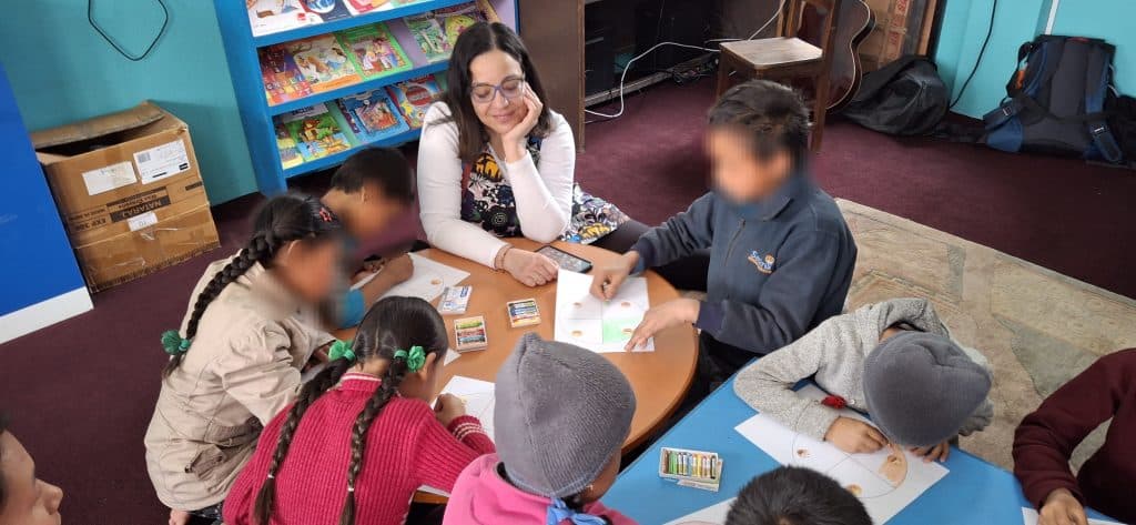 A facilitator seated at a low table with children in a room lined with bookshelves