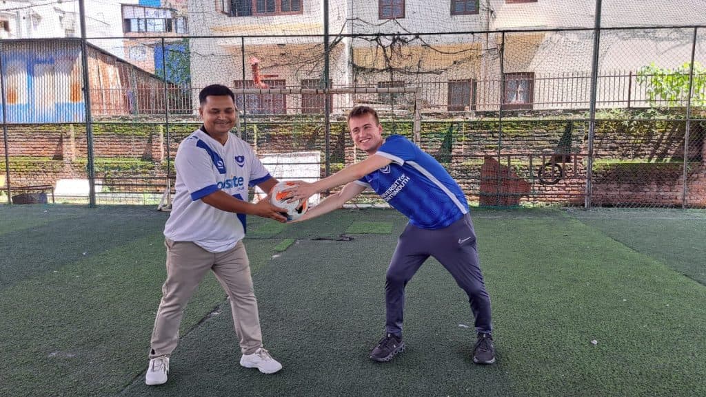 Two people playing football together on a small artificial-turf pitch