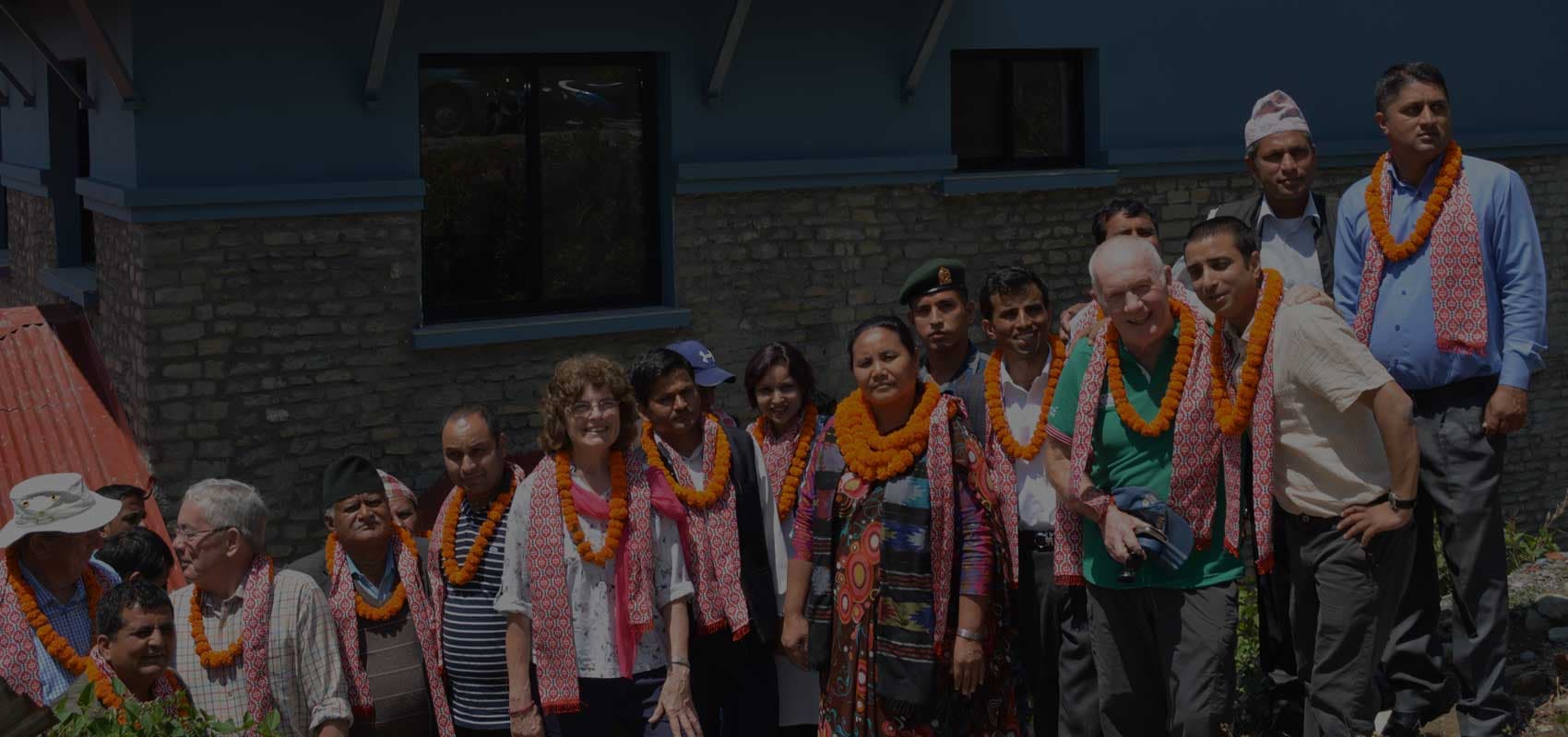 A group of Nepali hosts and international visitors wearing marigold garlands outside a building