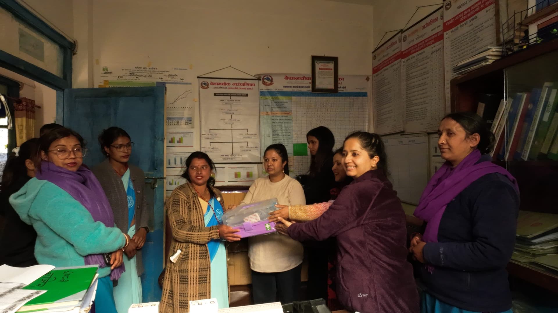 Women handing over a package of supplies across a desk inside a health post office
