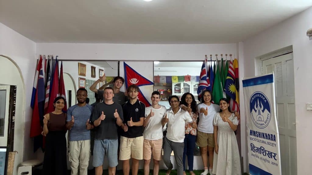 A group of international volunteers standing together in an office beneath a row of national flags