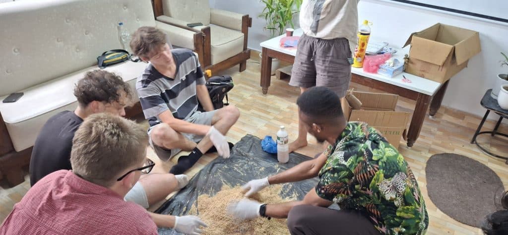 A group seated on the floor of a room sorting natural fibre material from a large sheet