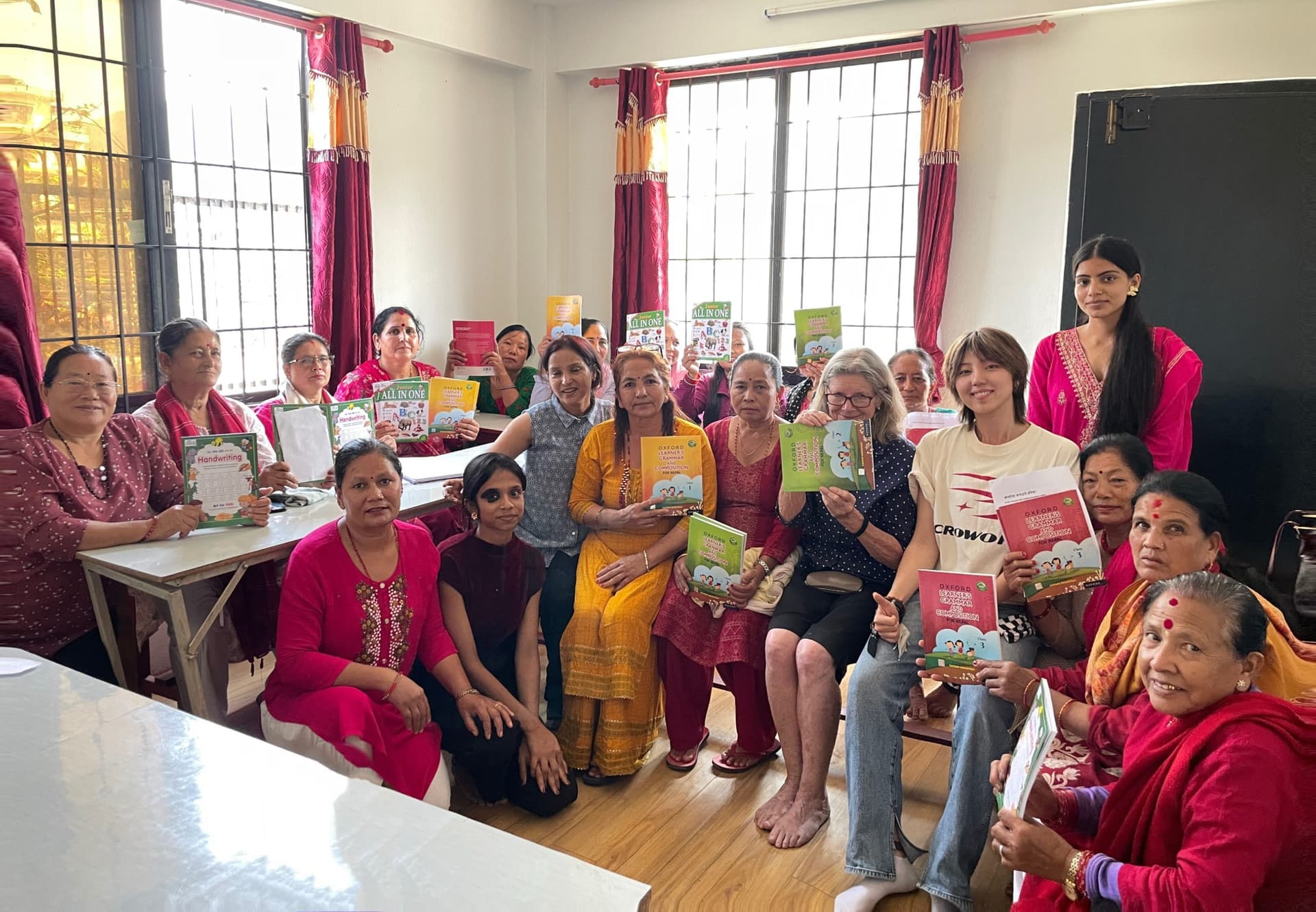 Women and facilitators standing and seated together in a hall, holding printed booklets and learning materials