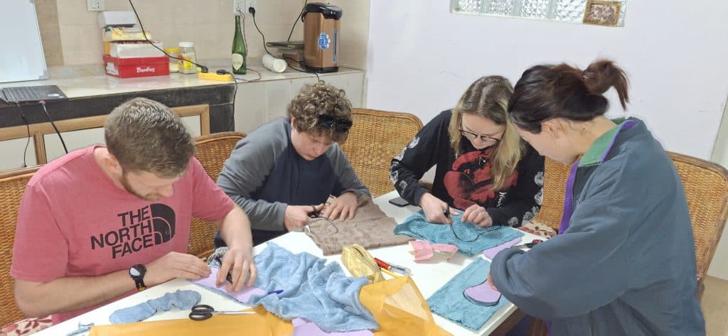 Four people around a table cutting and pinning fabric pieces for reusable pads