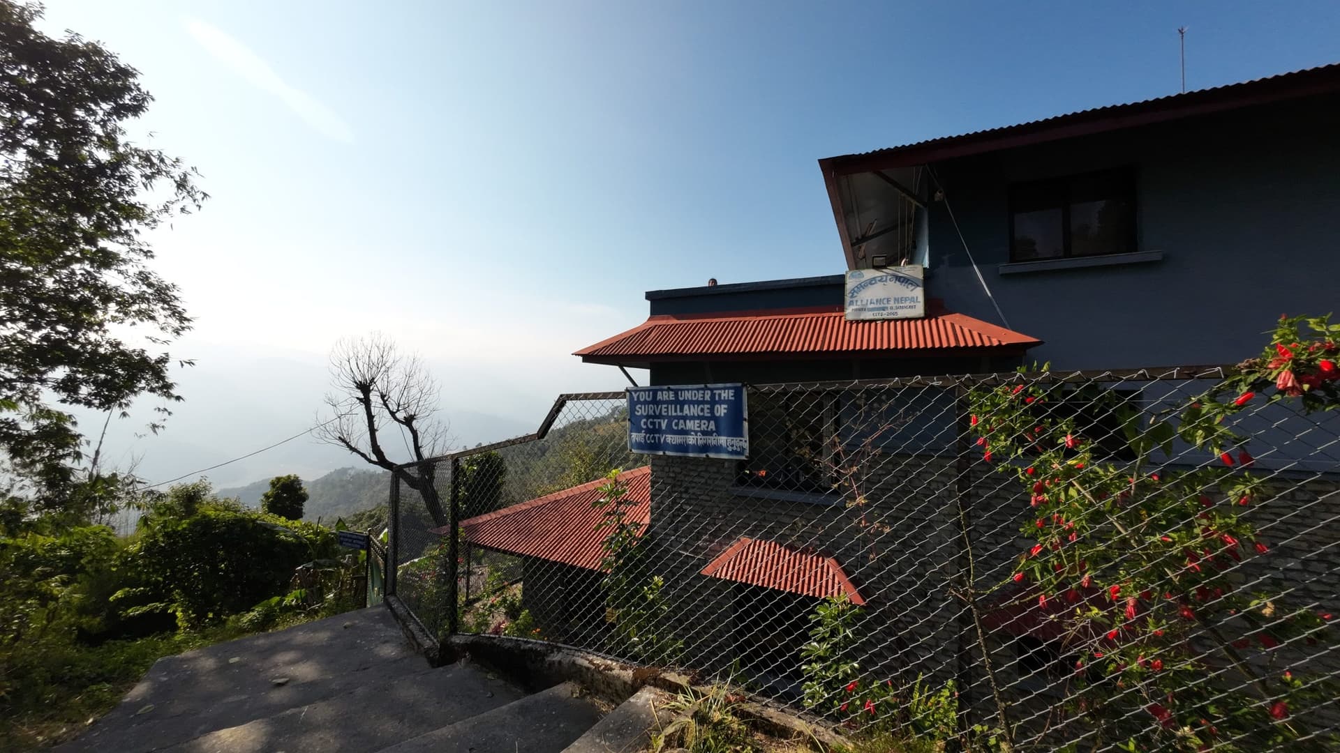 A hillside building with a red-tiled roof and a signboard, overlooking a valley at Sarangkot