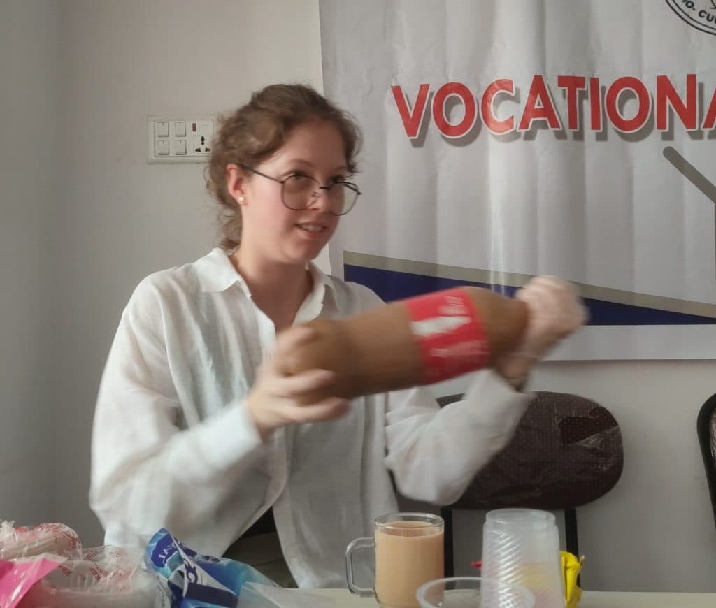 A participant at a table holding a wrapped handmade product in front of a vocational training banner