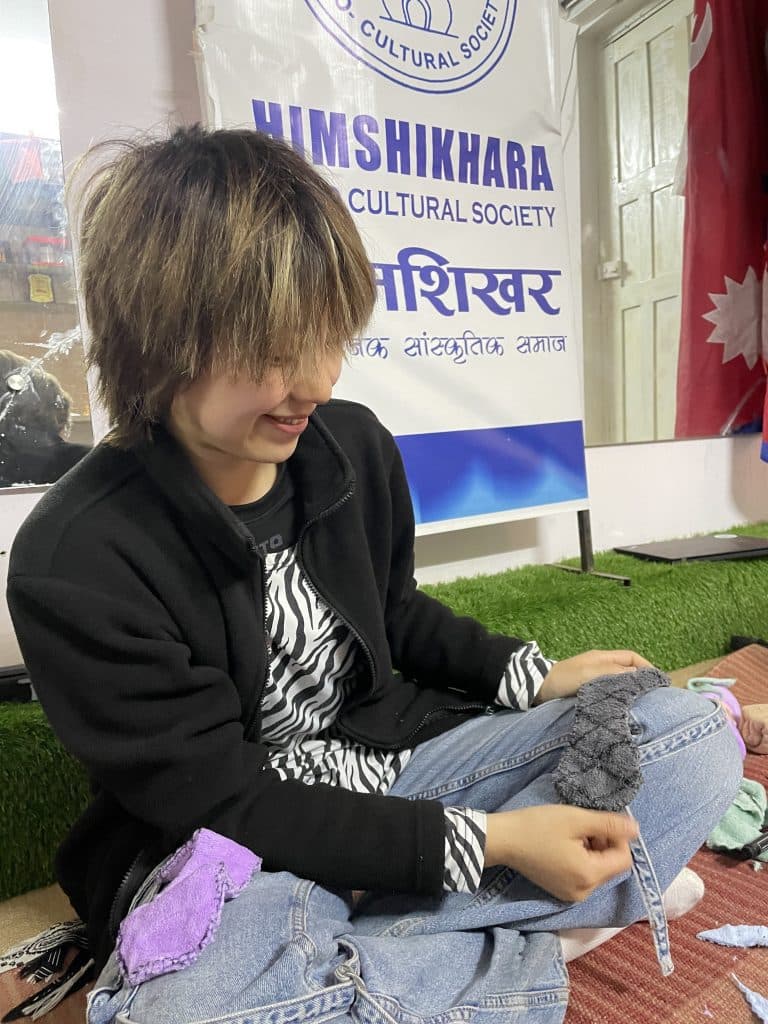 A volunteer seated on the floor stitching fabric in front of an organisation banner