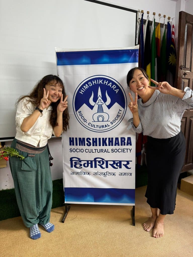 Two volunteers standing either side of a HISCUS banner printed in English and Nepali