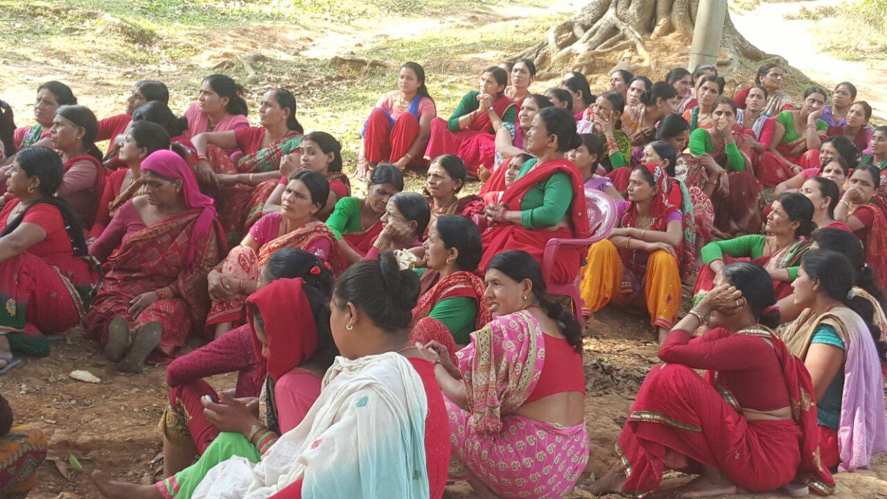A large group of women seated together on the ground under a tree during a community session in Nepal